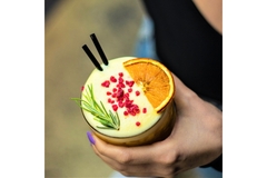 Image A woman holds a colorful drink with foam on top.